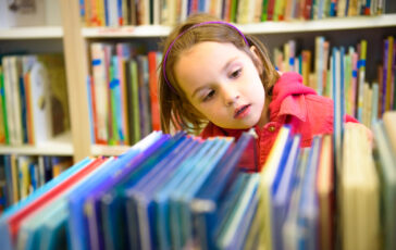 Little Girl Is Choosing A Book In The Library